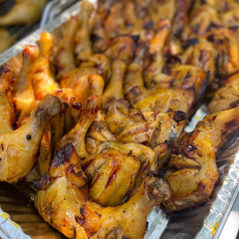 Close-up of numerous golden-brown grilled chicken pieces, some with charred skin, in a metal tray.