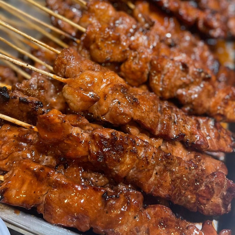 Close-up of numerous glistening Filipino pork skewers, known as Mang Eton BBQ, on display.