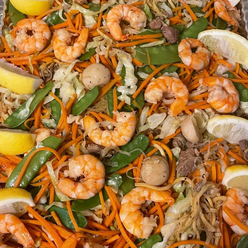 Close-up of Mang Eton's Pancit, a Filipino noodle dish with shrimp, vegetables, and lemon wedges.