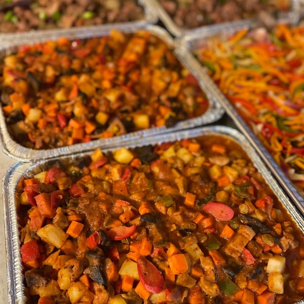 Multiple foil trays filled with colorful Filipino dishes, including a stew with vegetables and a noodle dish.