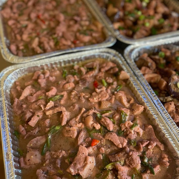 Multiple foil trays filled with Filipino Bicol Express, featuring pork, green chilies, and red chilies.