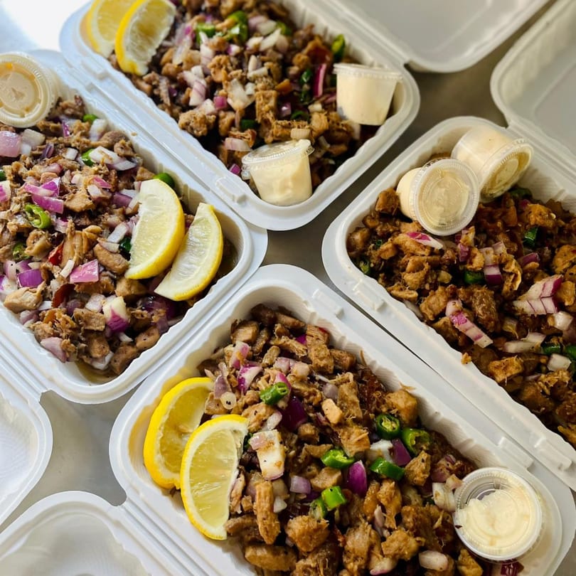 Four takeout containers of Mang Eton Filipino sisig with lemon wedges, onions, and peppers.