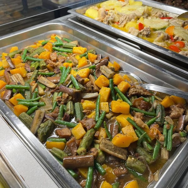 Two buffet trays of Filipino food, with a vegetable and meat stew in the foreground.