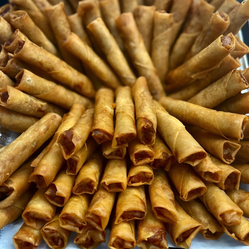 A close-up of numerous golden-brown Filipino lumpia rolls, arranged in a circular pattern.