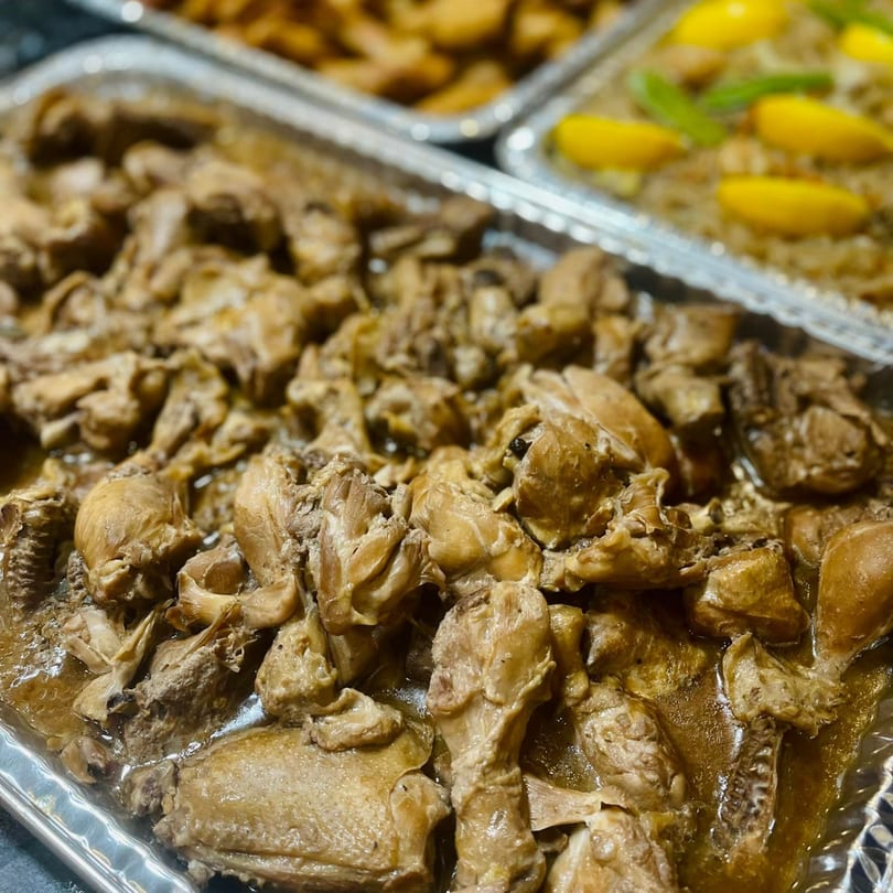 Close-up of Mang Eton Filipino Food's chicken adobo in a foil tray, with another dish in the background.