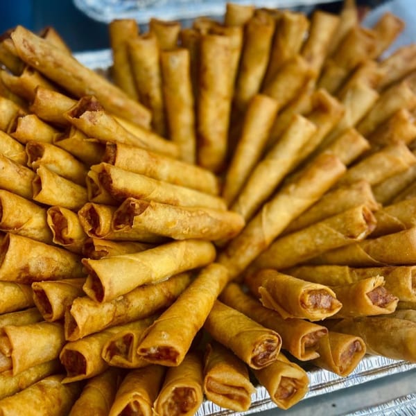 A large platter of golden-brown Filipino lumpia, or fried spring rolls, arranged in a circular pattern.