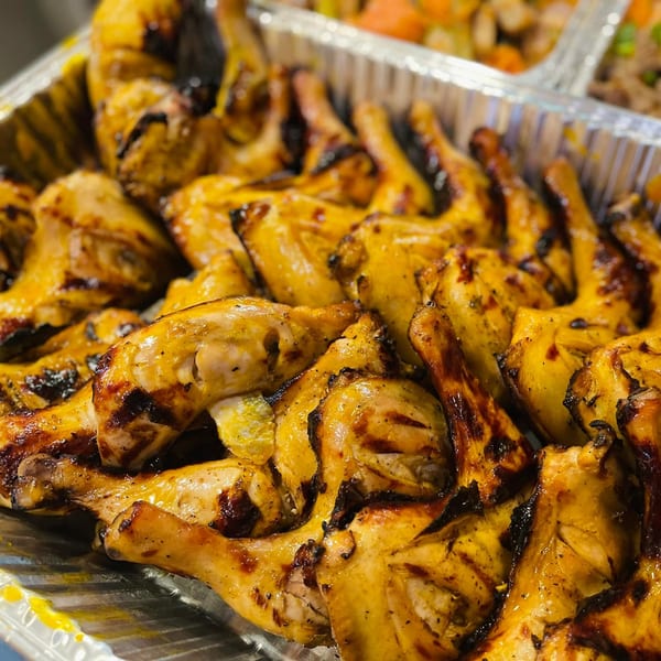 Close-up of golden-brown grilled chicken pieces with charred marks in a foil tray.