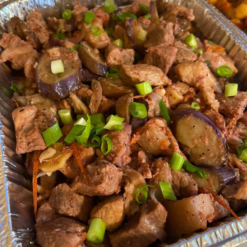 Filipino pork and eggplant adobo, garnished with green onions, in a foil takeout container.